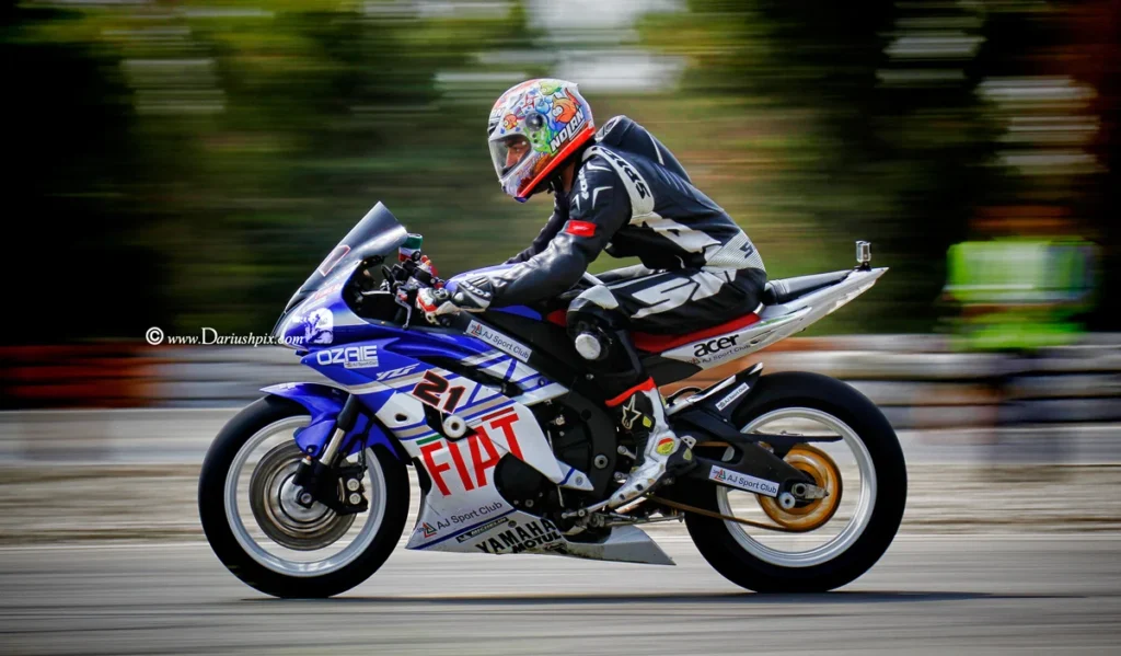 Professional panning shot of a sport bike accelerating on a track, featuring a sharp subject with a motion-blurred background and rotating wheels at high speed.